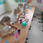 Uczniowie siedzą w ławkach i jedzą sałatkę.