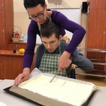 Nauczyciel i uczeń kroją nożem ciasto francuskie leżące na blaszce.