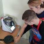 Uczeń podnosi ze stołu pokrywę do garnka termomiksu.