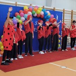 Grupa uczniów w czerwonych ubraniach stoi na sali gimnastycznej