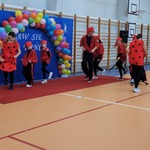 Grupa uczniów w czerwonych ubraniach tańczy na sali gimnastycznej