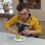 Uczeń siedzi  przy stole i obiera gruszkę obieraczką.
