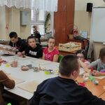 Grupa uczniów siedzi wokół stołu na którym leżą narzędzia do obróbki gliny.