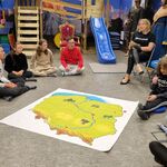 Grupa uczniów siedzi na podłodze.Przed nimi leży mapa Polski..