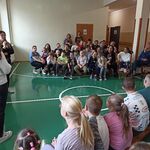 Społeczność szkolna siedzi na ławeczkach i słuch opowieści pań wolontariuszek.