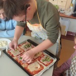 Uczeń kladzie kawałek papryki na pizzę leżącą na blaszce.