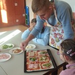 Uczeń kladzie ser na pizzę leżącą na blaszce.