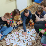 Dwóch chłopców i dwie dziewczynki siedzą na dywanie, jedna dziewczynka siedzi na krześle. Na dywanie przed uczniami, leżą ułożone karteczki z bohaterami bajek.