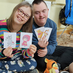 Uczeń i uczennica siedzą na dywanie. W ręku trzymają obrazki z postaciami z bajek. Uczeń siedzi na dywanie. W ręku trzyma obrazek z postacią z bajki Świnka Pepa.
