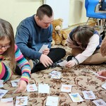 Dwie dziewczynki i dwóch chłopców siedzą na dywanie. Przed nimi lezą karteczki z bohaterami bajek. Uczniowie szukają dwóch takich samych bohaterów.