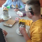 Uczniowie siedzą przy stole i tarkują czekoladę na tarce.