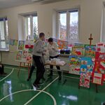Nauczycielka wręcza nagrodę uczestnikowi konkursu. W tle wystawa prac konkursowych.