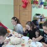Grupa uczniów siedzi wokół urodzinowego stołu i je tort.