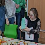 Koledzy i koleżanki składają życzenia jubilatce siedzącej za stołem.