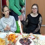 Koledzy i koleżanki składają życzenia jubilatce siedzącej za stołem.