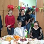 Grupa uczniów stoi za stołem urodzinowym przy którym siedzi jubilatka i jej koleżanka.