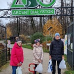Trójka uczniów stoi przed wejściem do zoo. Nad nimi zielony duży napis  Akcent Białystok . W rękach trzymają reklamówki z żołędziami.