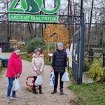 Trójka uczniów stoi przed wejściem do zoo. Nad nimi zielony duży napis  Akcent Białystok . W rękach trzymają reklamówki z żołędziami.