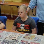 Trójka uczniaków siedzi za stołem. Przed nimi leżą na gazetach figurki z gliny.