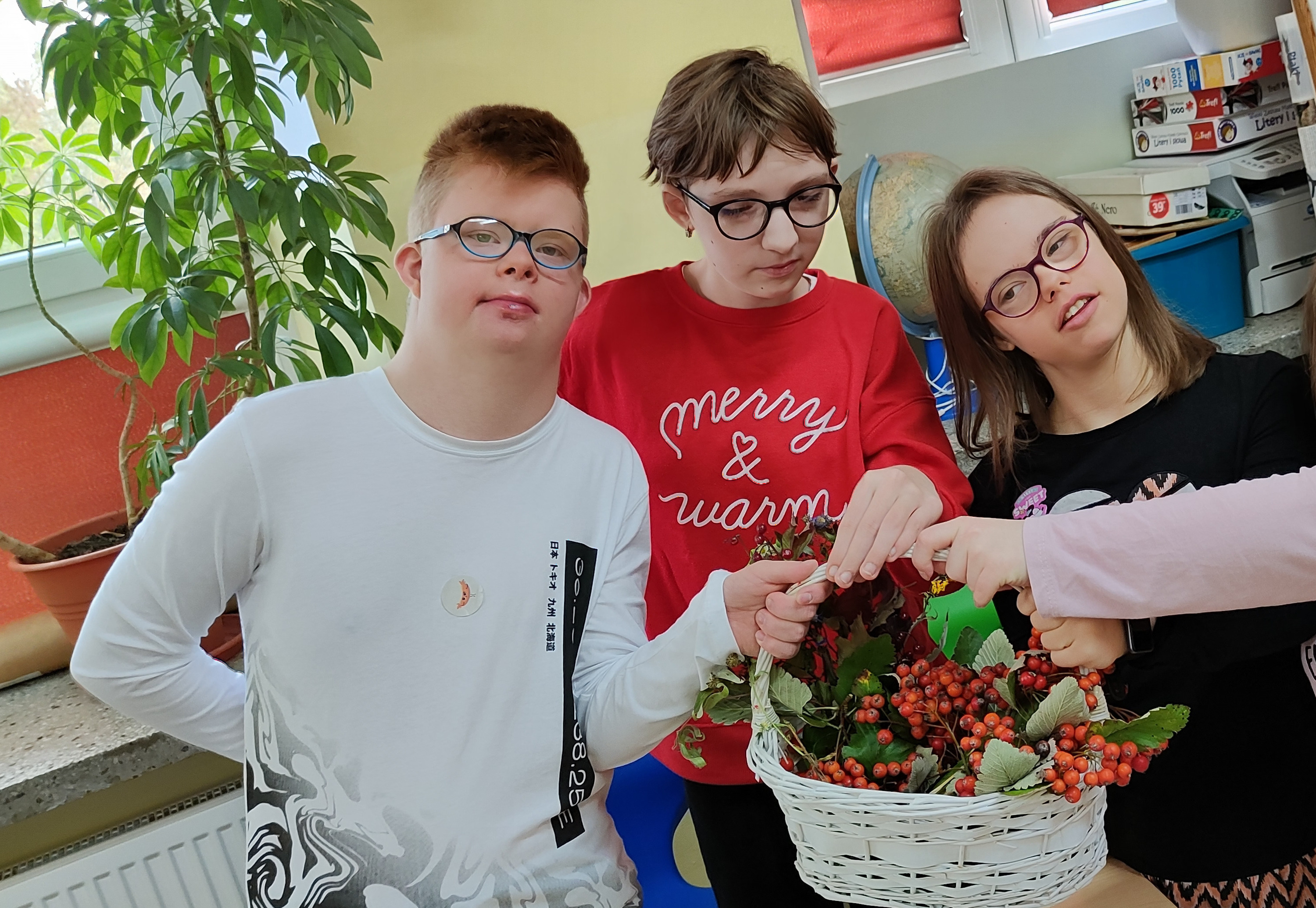 Uczniowie stoją przy ławce. W ręku trzymają ułożona przez siebie w koszyku jesienna kompozycję z darów jesieni.