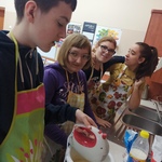 Trzy uczennice patrzą na kolegę mieszającego ciasto mikserem w misce.
