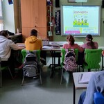 Uczniowie siedzą w ławkach i oglądają prezentację wyświetlana na tablicy interaktywnej.