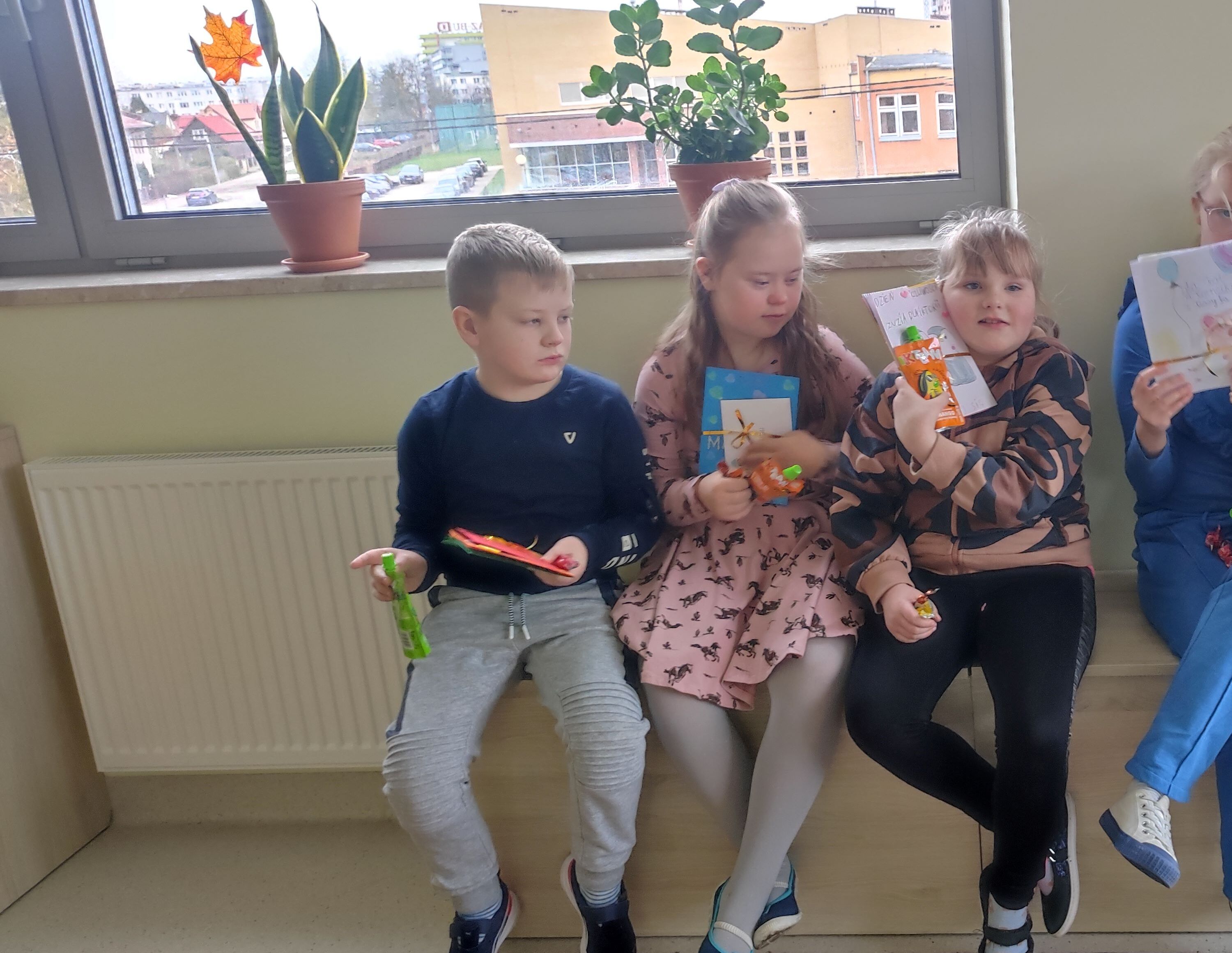 Pięcioro uczniów siedzi na ławeczce. Wszyscy trzymają w rękach laurki.