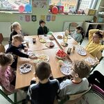 Uczniowie siedzą przy stole, jedzą słodycze i przekąski.