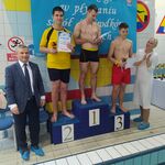 Zawodnicy na podium oraz organizatorzy zawodów pływackich.