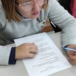 Uczennica siedzi przy stole i rozwiązuje test.