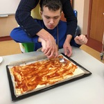 Uczeń z pomocą nauczycielki smaruje spód pizzy keczupem.