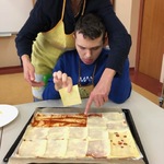 Uczeń z pomocą nauczyciela kładzie plaster sera na pizzy.