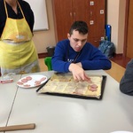 Uczeń kładzie plasterki kiełbasy na pizzę.