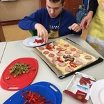 Uczeń kładzie kawałki papryki na pizzę.
