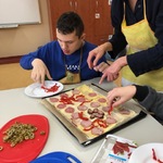 Uczeń kładzie kawałki papryki na pizzę.