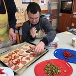 Uczeń kładzie kawałki papryki na pizzę.