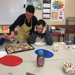 Uczeń obserwuje nauczycielkę posypującą pizzę przyprawą z torebki.