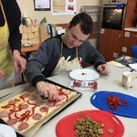 Uczeń kładzie kawałki papryki na pizzę.