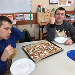 Uczniowie siedzą przy stole. Przed nimi stoją talerze i pizza na blaszce.