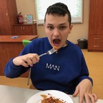 Uczeń siedzi przy stole i je pizzę.