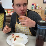 Uczeń siedzi przy stole i je pizzę.
