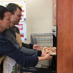 Uczeń z pomocą nauczycielki wkłada blachę z pizza do piekarnika.