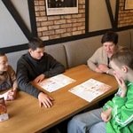 Nauczycielka i trzech uczniów siedzą przy stoliku. Przed nimi leży karta z menu.