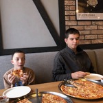 Uczniowie siedzą za stołem i jedzą pizzę.