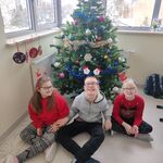 Trójka uczniów siedzi na podłodze pod choinką.