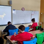 Uczniowie siedzą przy stolikach i rozwiązują karty pracy.