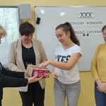 Pani Dyrektor częstuje uczennicę czekoladką. Obok stoi nauczycielka i mama uczennicy.