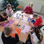 Uczniowie siedzą wokół stołu i dekorują pierniczki.