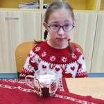 Uczennica siedzi za stołem. Przed nią stoi świąteczny kubek
