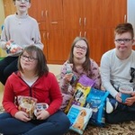 Grupa uczniów siedzi na dywanie. Przed sobą trzymają torby z karma dla zwierząt.